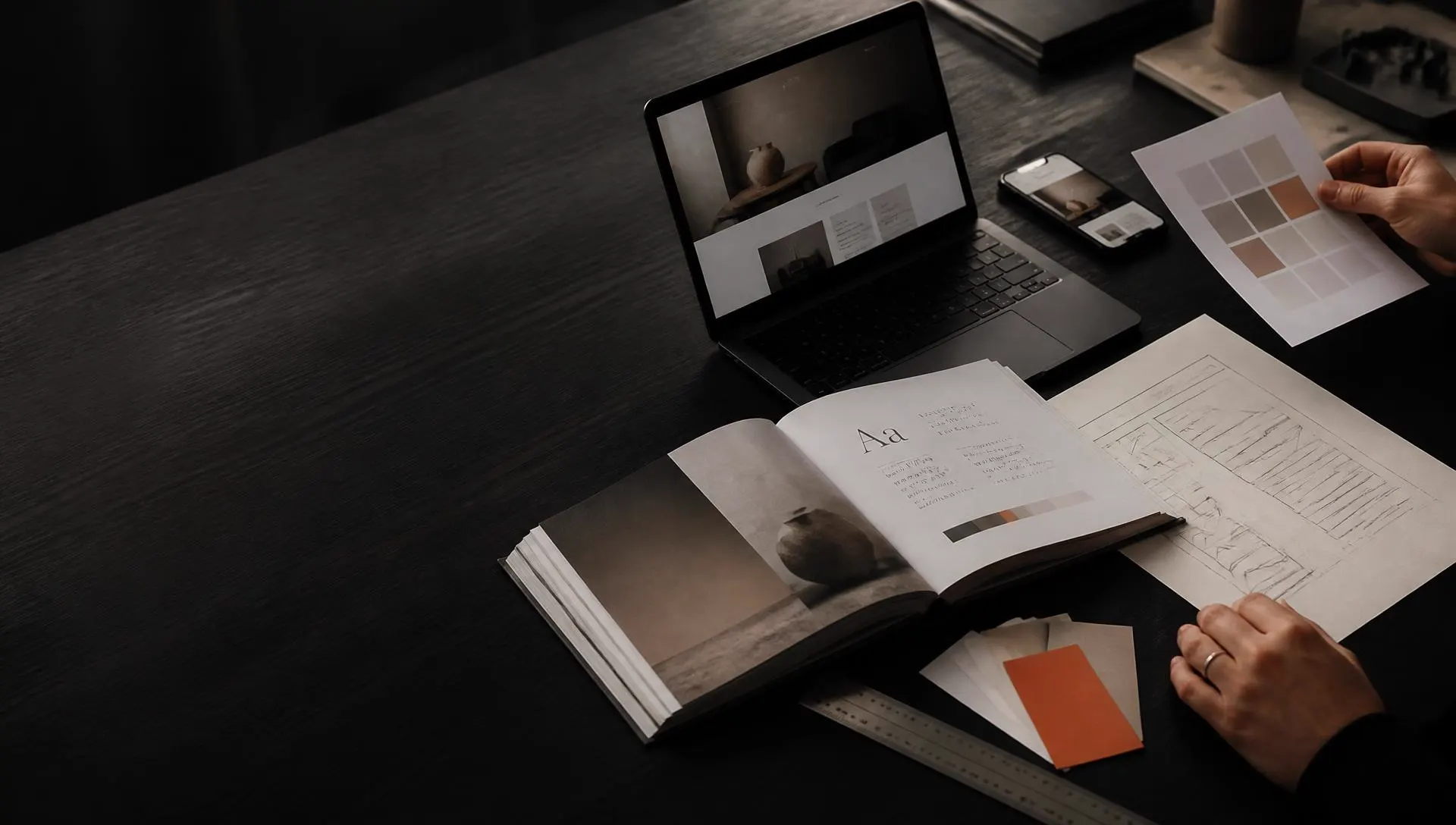 Mesa de trabajo de un estudio creativo con brand book, muestras de color y un diseño web en pantalla